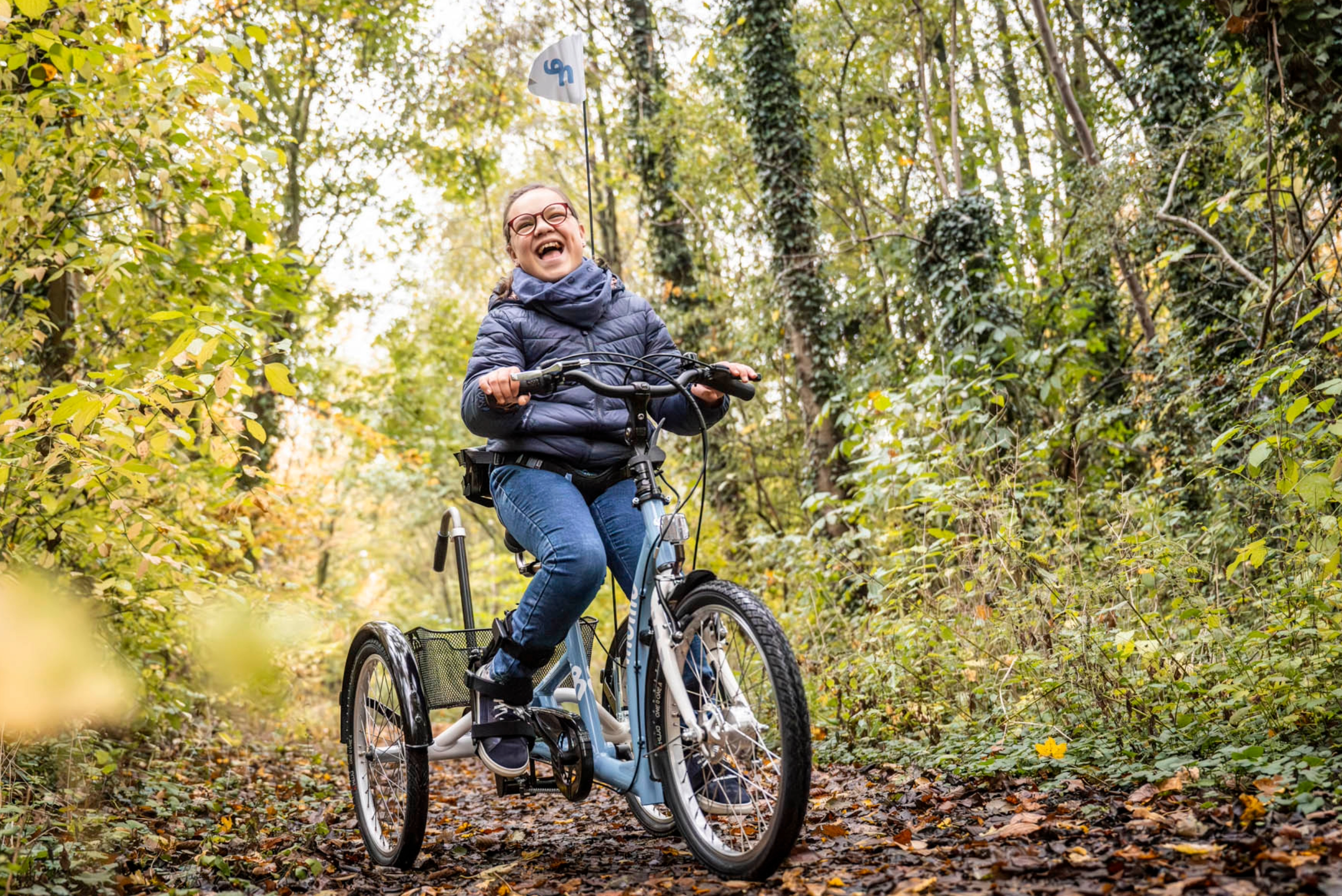 Ein Mädchen mit Behinderung sitzt auf dem momo dreirad. Einem Fahrrad für Kinder mit Behinderung.